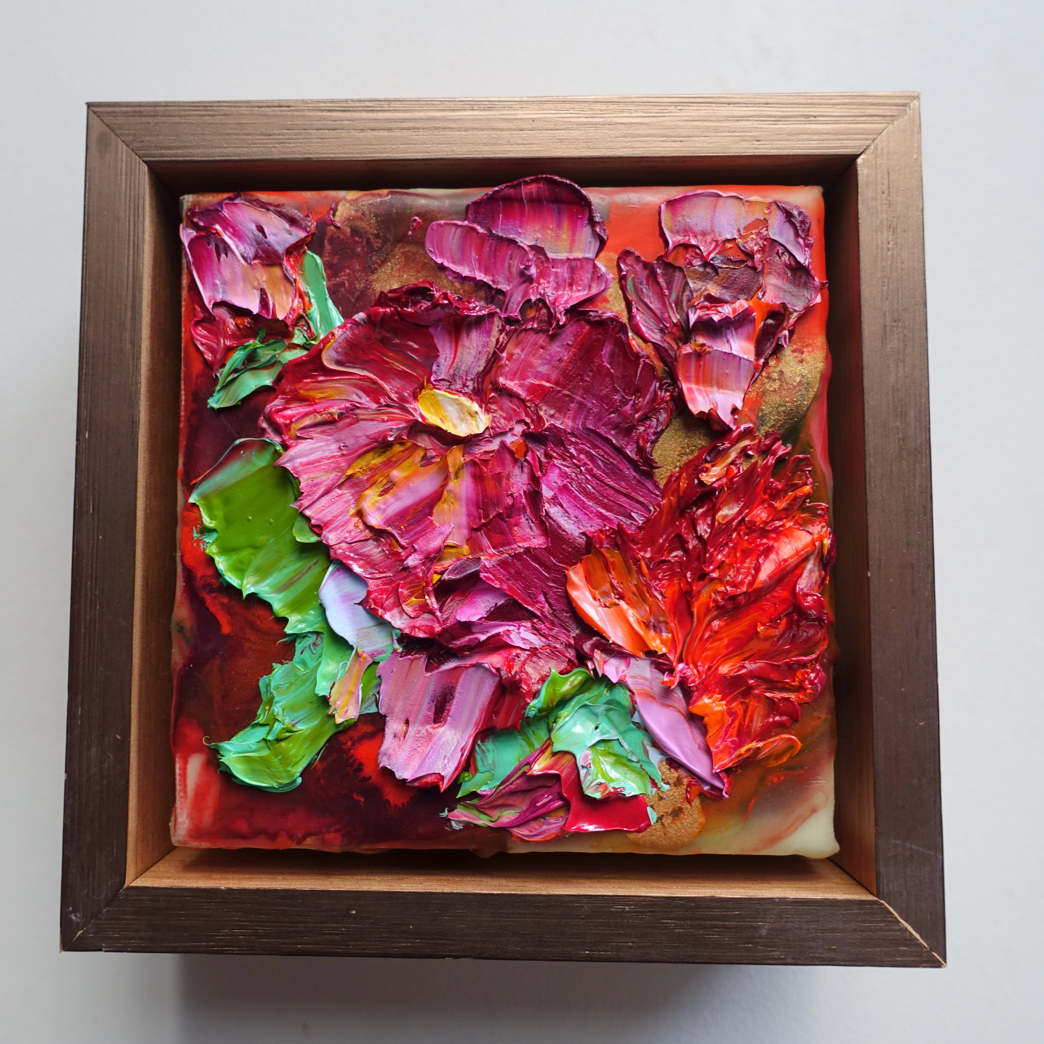 A cut oil painting with tones of hot pink, red and green, framed in light oak with gold face