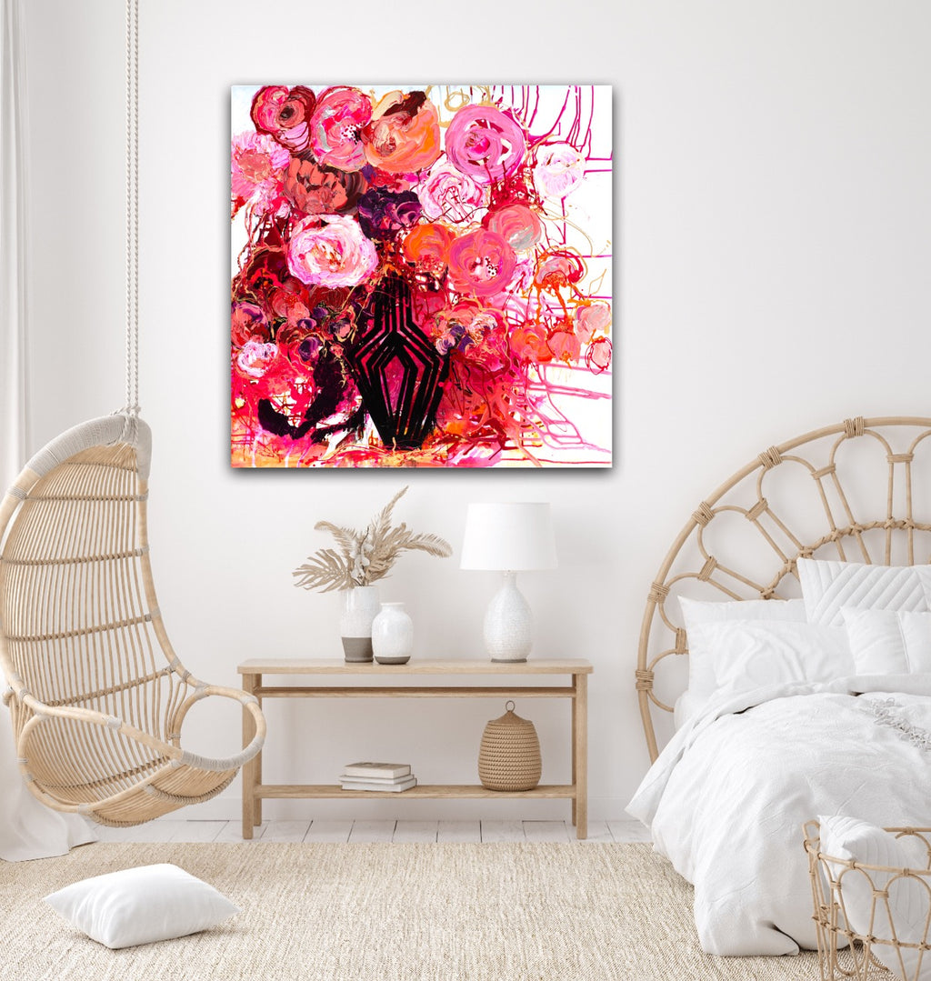 Buds & Blooms is a vibrant mass of red and pink blooms in a black vase against a white wall.