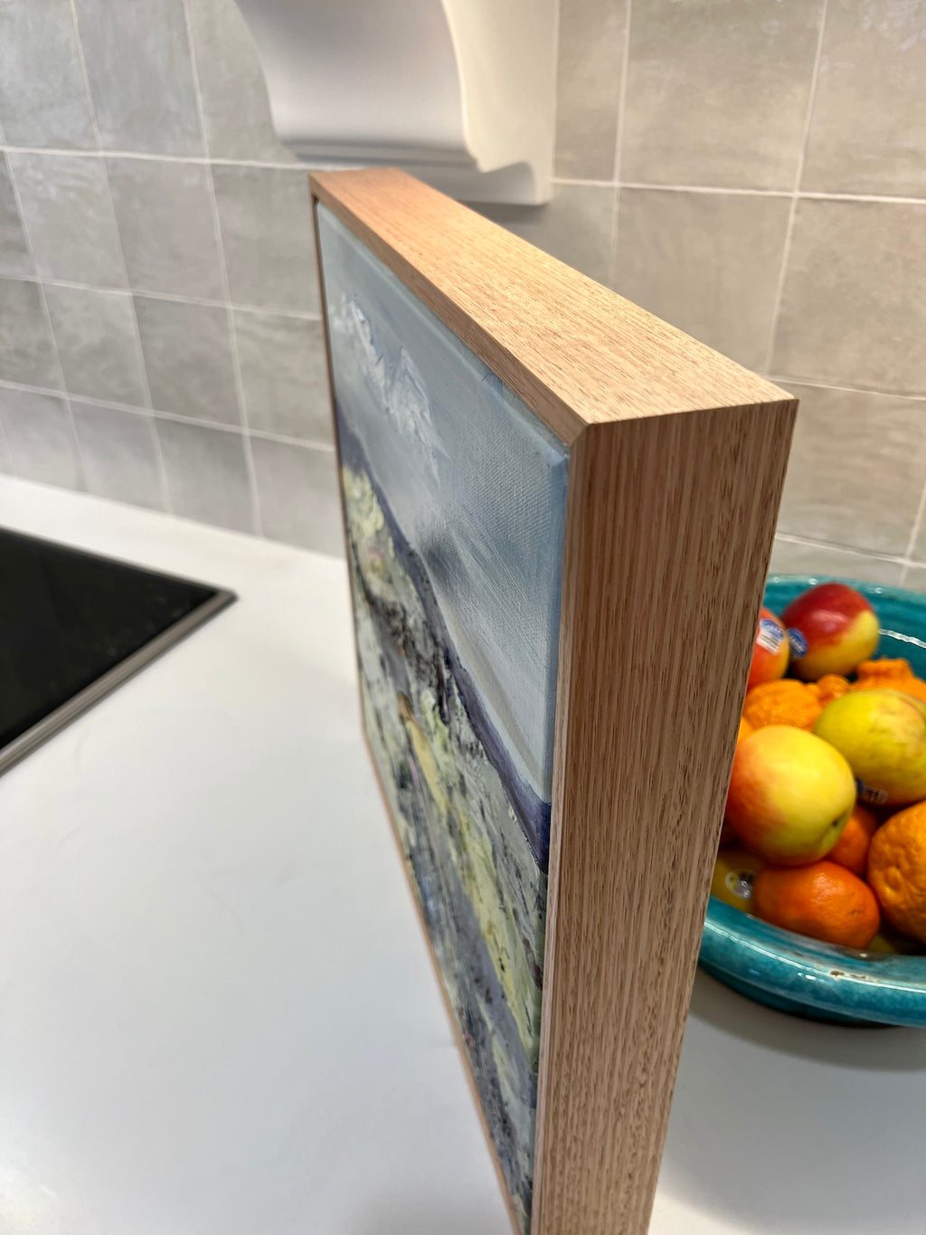 Abstract oil painting of a country landscape with steep hills and lots of colour, yellow, pink, green and blue against a pale blue sky with white clouds. Side view.