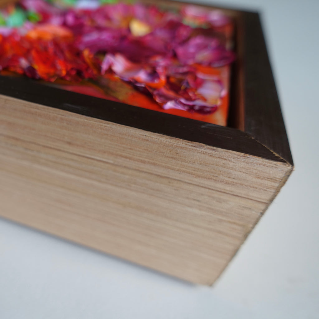 Side view of a cute oil painting with texture in tones of hot pink, red and green, framed in oak with a gold face.