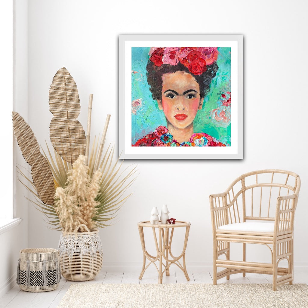 A beautiful and colourful print of Frida Kahlo with red and pink flowers in Frida's hair against a turquoise and aqua background, framed in white timber.