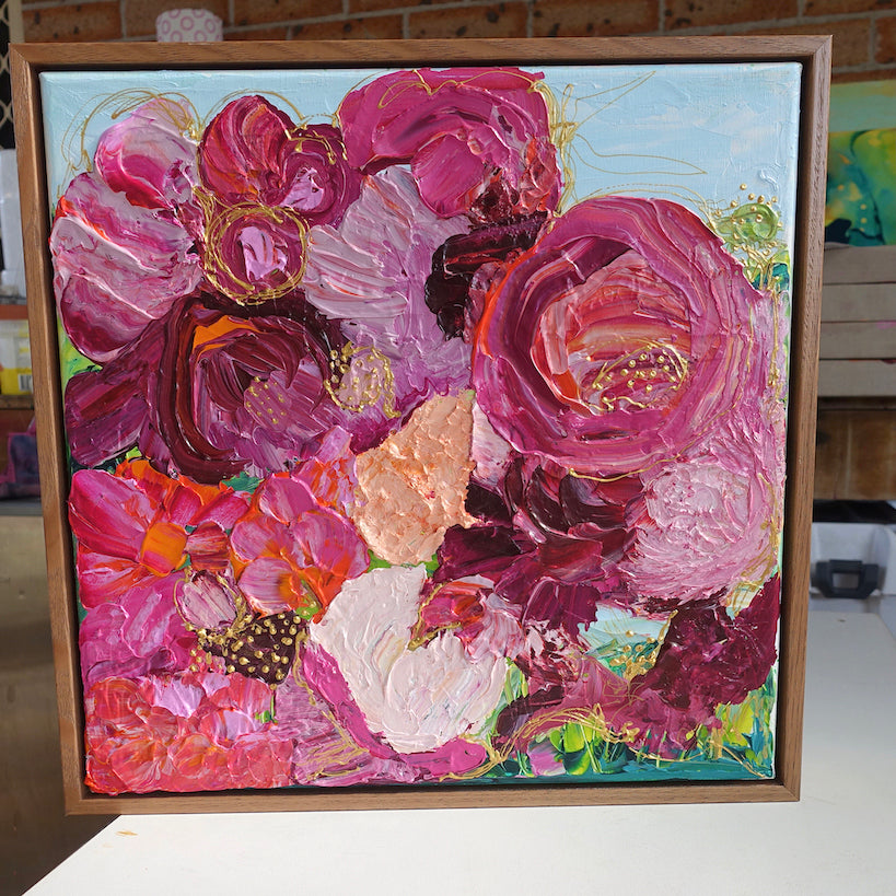 A painting of a gorgeous bunch of florals in all shades of pink, entwined with gold thread on a pale blue background framed in Tasmanian Oak.