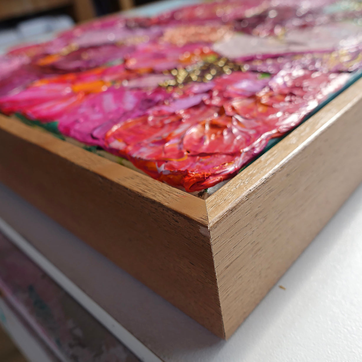 Close up view of an original painting of a gorgeous bunch of florals in all shades of pink, entwined with gold thread on a pale blue background.