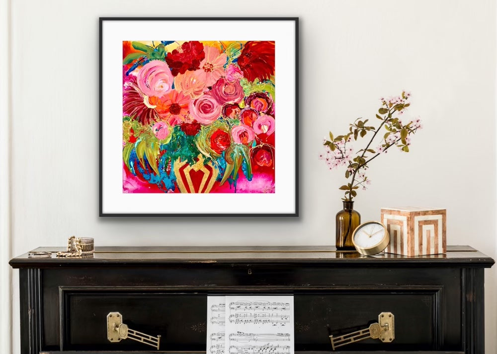A stunningly beautiful print of a mass of blooms in shades of pink, red outlined in gold, in a gold vase against a hot pink background, in a timber frame.