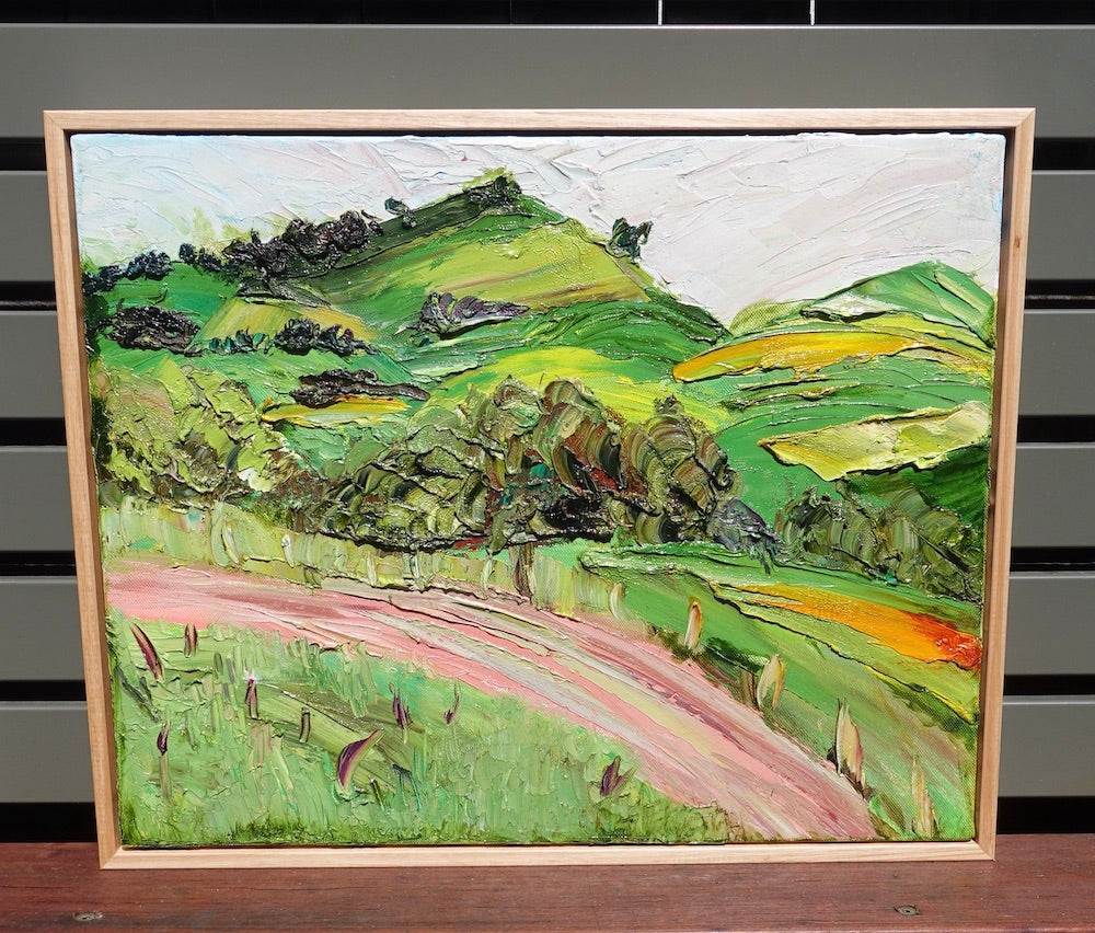 Abstract landscape of rolling green and yellow hills and a winding pink road. Framed view.