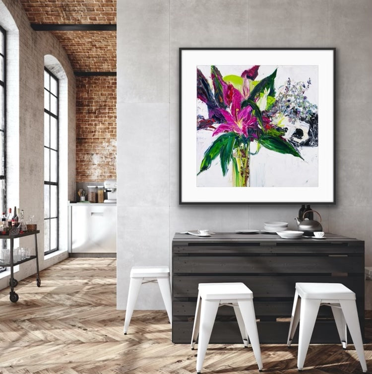 A tall stemmed bloom in shades of violet and plum with greenery in a long, slim glass vase, framed in timber.