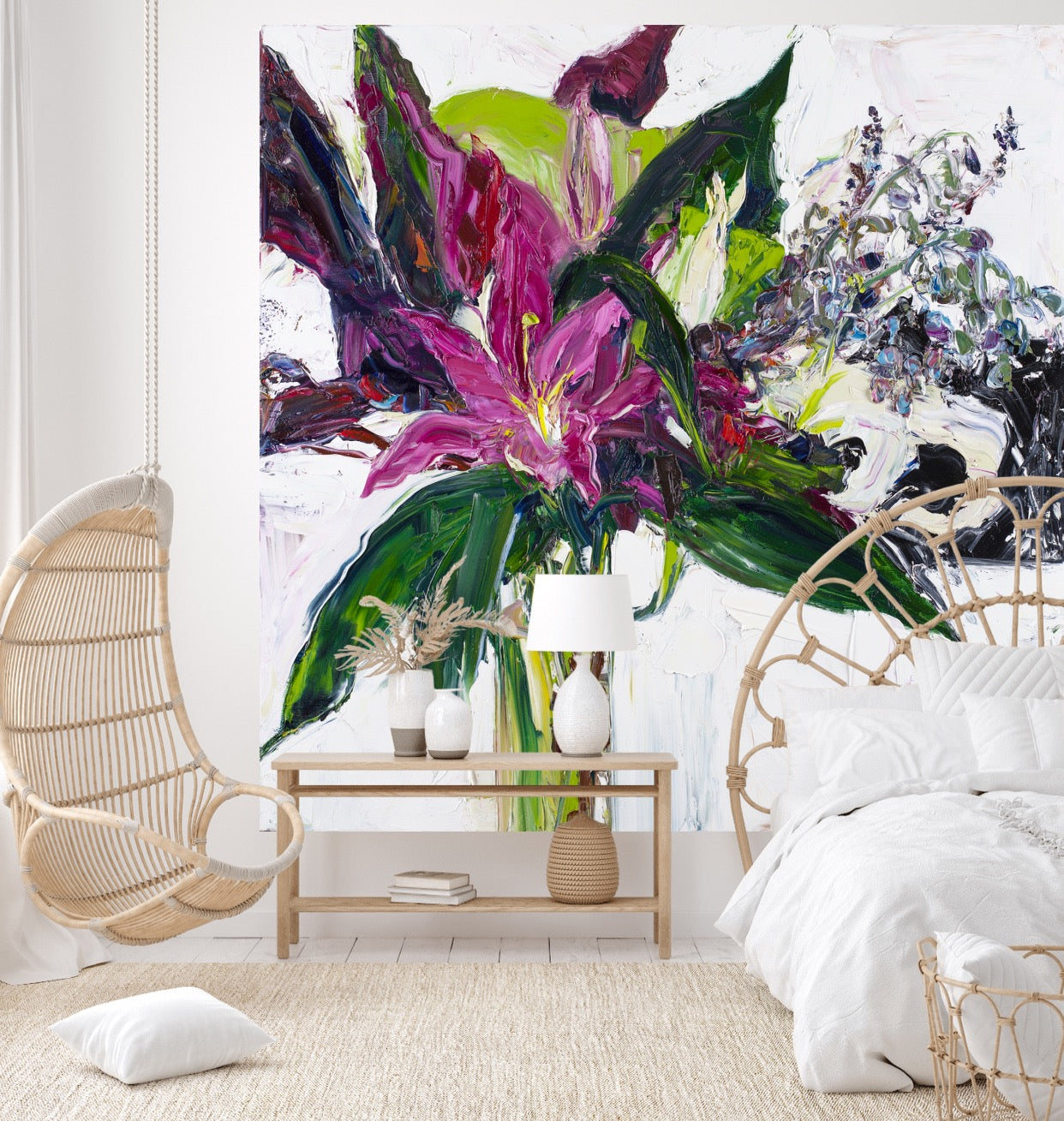 A tall stemmed bloom in shades of violet and plum with greenery in a long, slim glass vase, against a white wall.