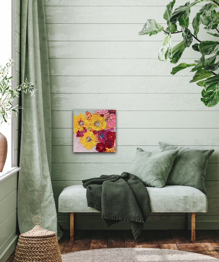 A painting of a pretty mass of blooms in shades of yellow, red, pale and deep pink, shown on a pale green panelled wall.