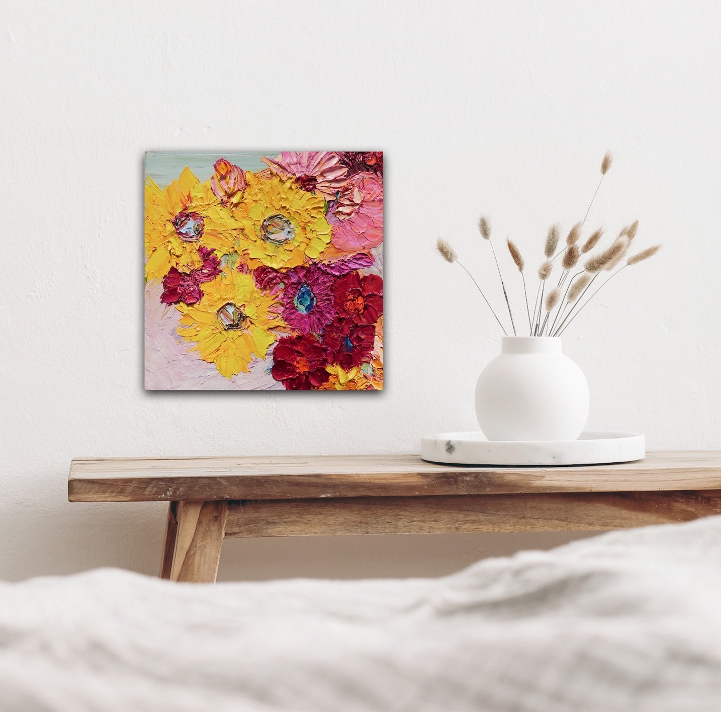 A painting of a pretty mass of blooms in shades of yellow, red, pale and deep pink, shown on a white wall.